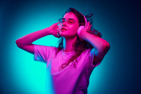 Caucasian woman's portrait isolated on blue studio background in multicolored neon light. Beautiful female model. Concept of human emotions, facial expression, sales, ad, fashion. Copyspace.
